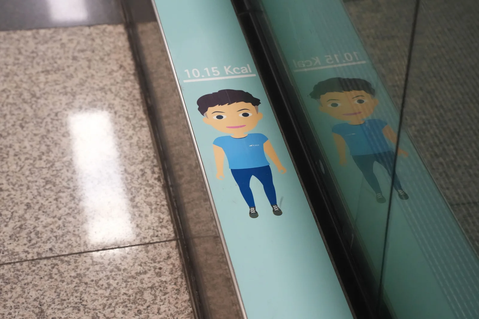 A cartoon figure in a blue shirt printed on the teal side panel of a moving walkway, above the text 10.15 Kcal.