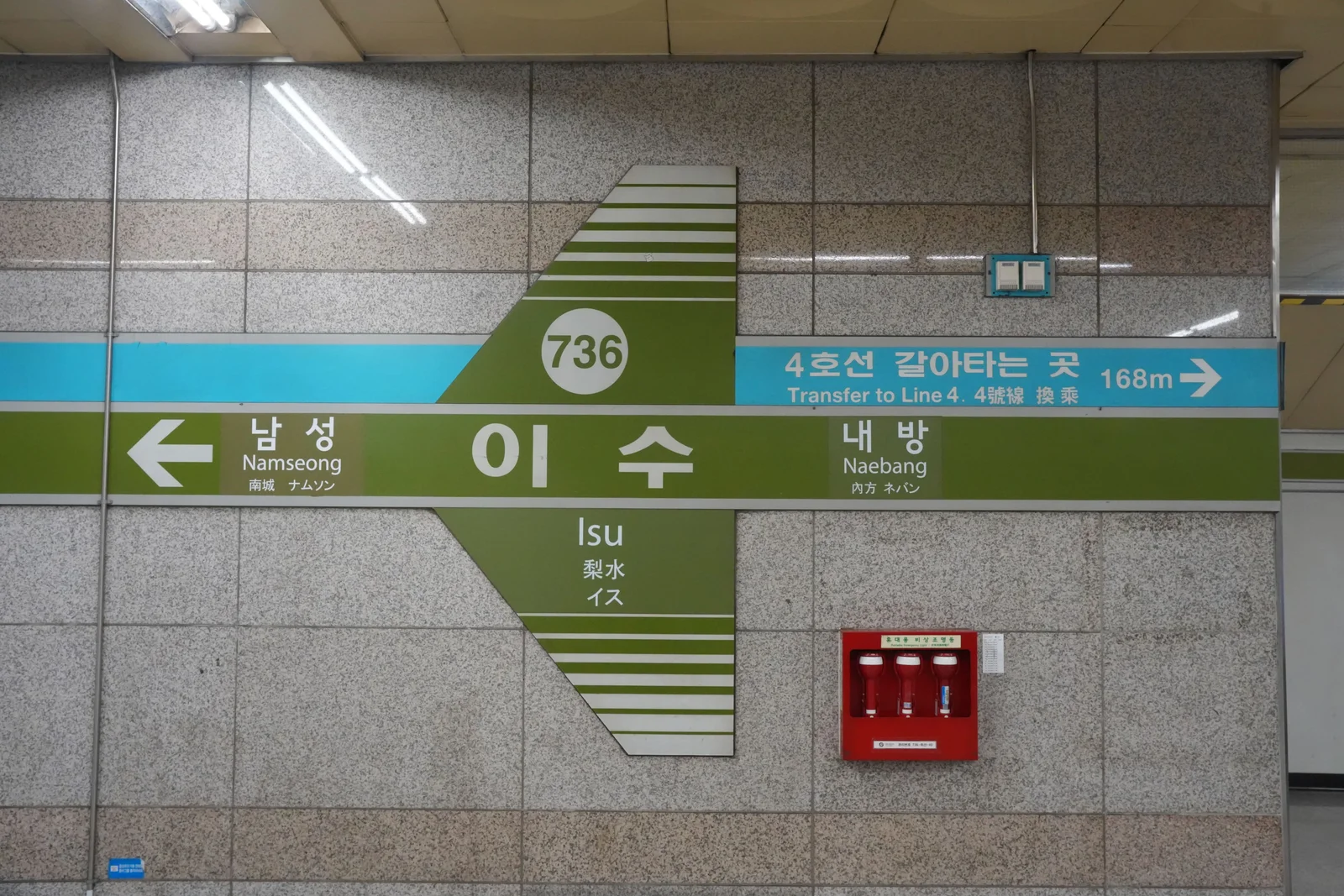 Platform wall sign at Isu station showing the station name in Korean, English, Chinese and Japanese, with Namseong to the left, Naebang to the right, and a blue band reading Transfer to Line 4, 168m.