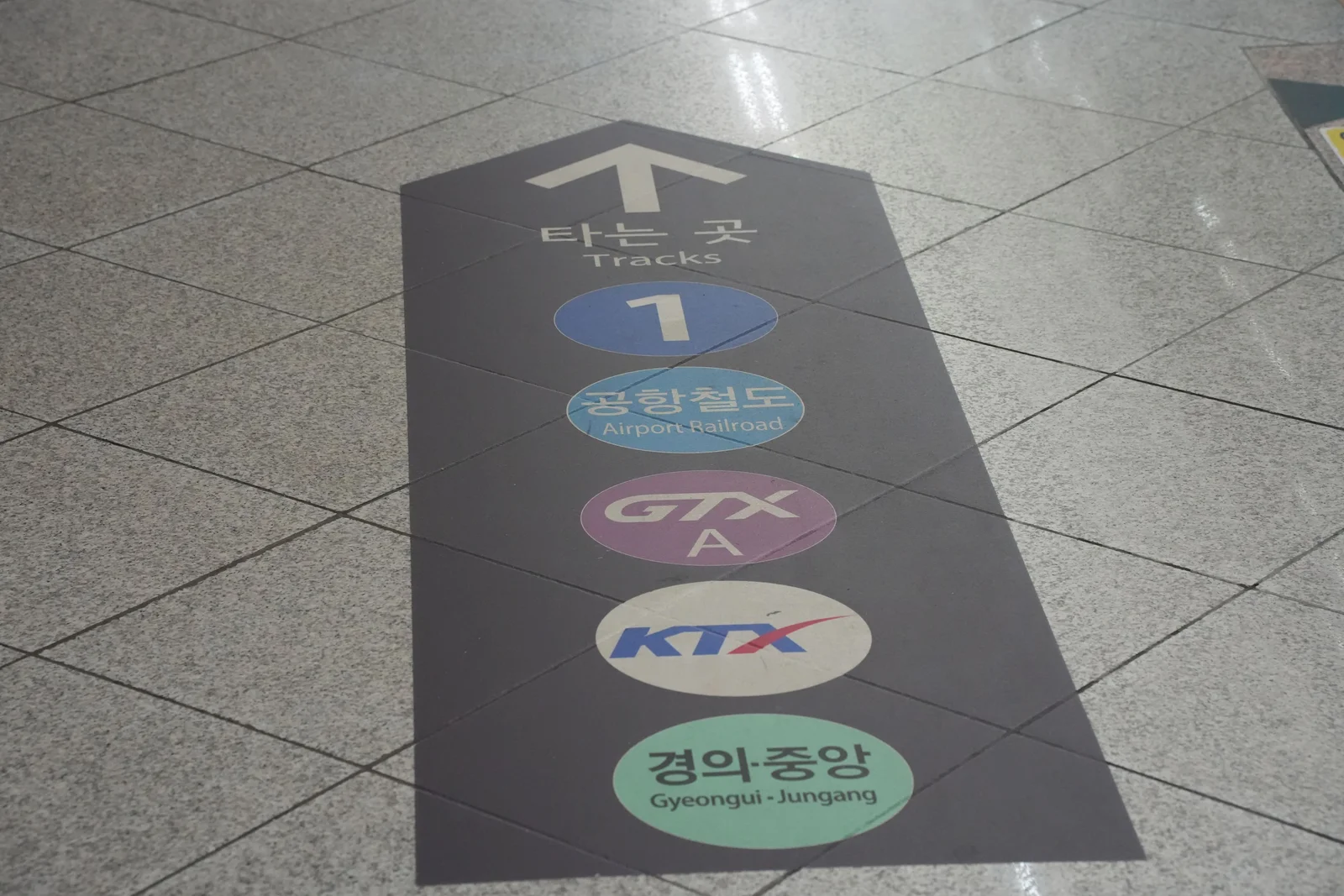 The same colored line markers printed on the station floor beneath an arrow and the word Tracks.