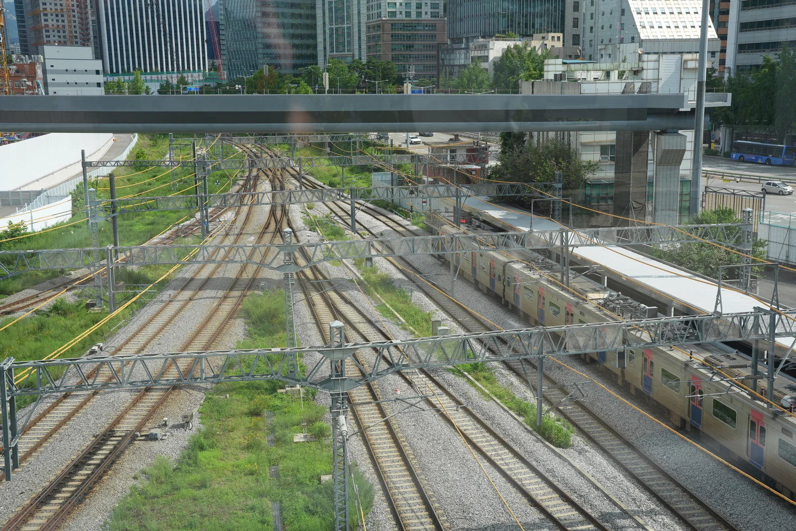 Looking down from the elevated walkway over the many converging tracks of the Seoul Station rail yard, with a commuter train at a platform.